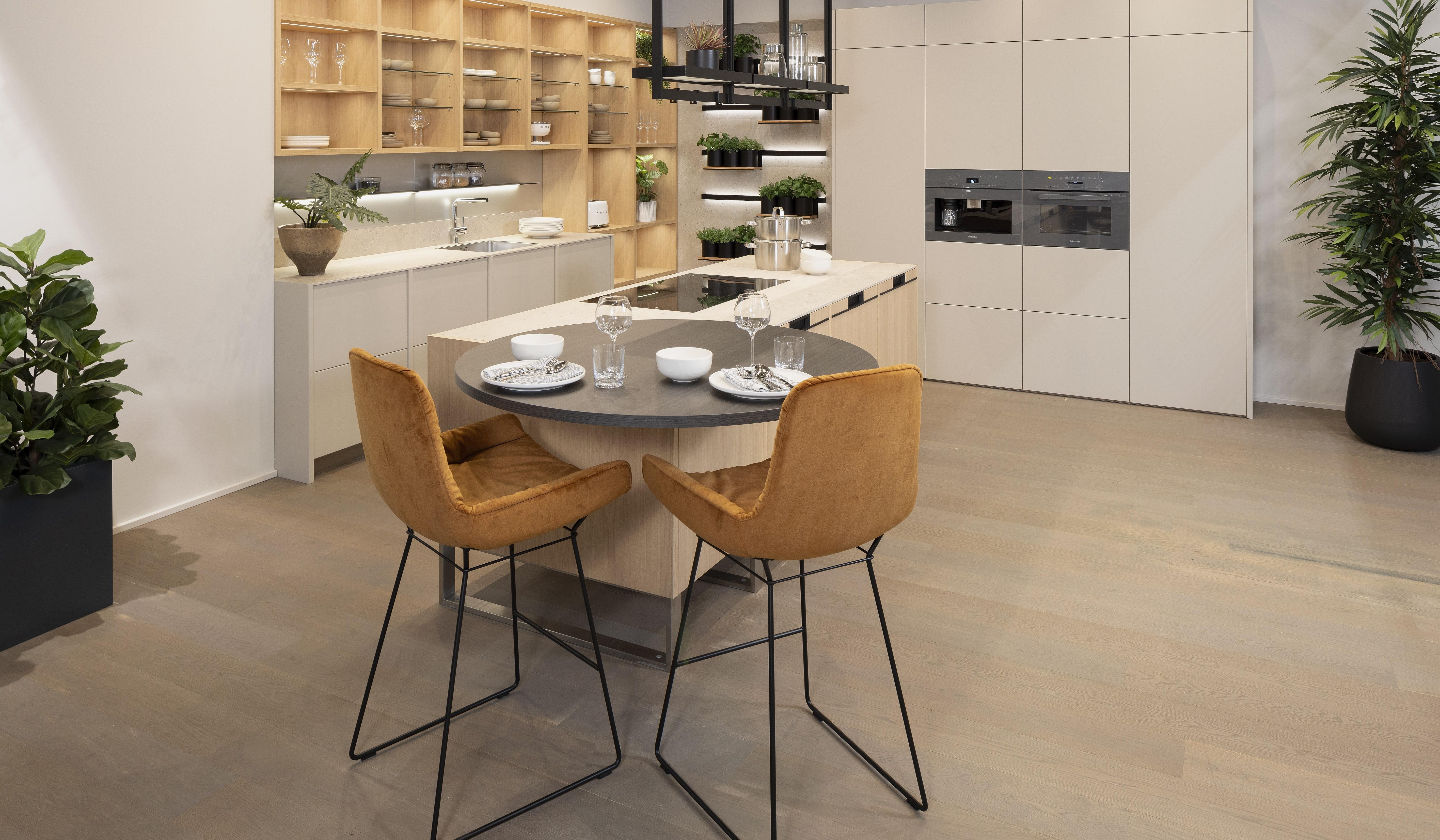 Moderne Küche mit runden Esstisch, zwei braunen Stühlen und grünen Pflanzen.