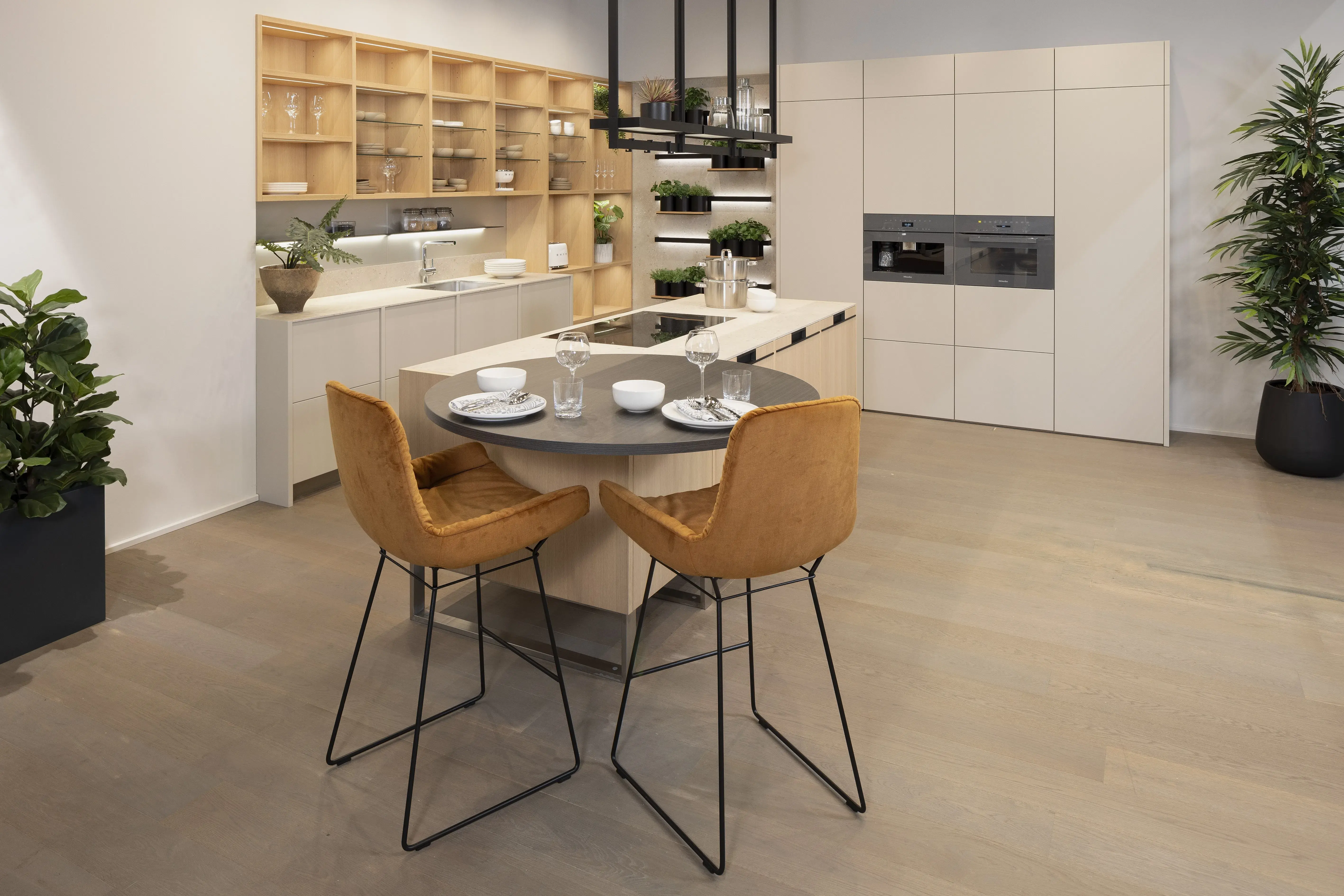 Moderne Küche mit runden Esstisch, zwei braunen Stühlen und grünen Pflanzen.